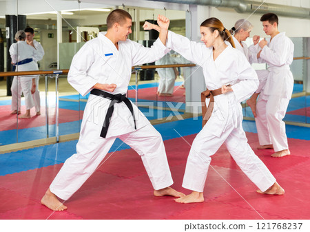 Man and woman in kimono sparring during group karate training Man and woman in kimono sparring during group karate training 121768237