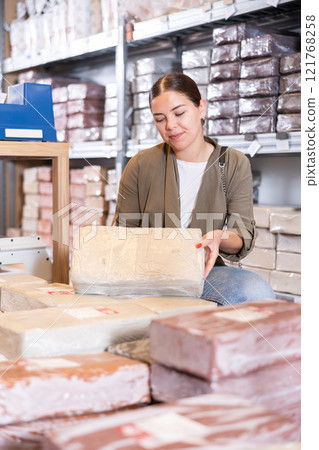 Female customer chooses briquettes with white clay in specialized store 121768258