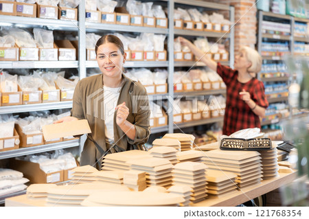 In pottery shop, positive woman chooses various wooden molds for future clay molding in her workshop 121768354