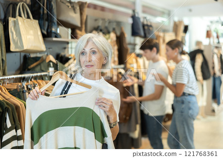 elderly lady carefully examines selection of sweaters 121768361