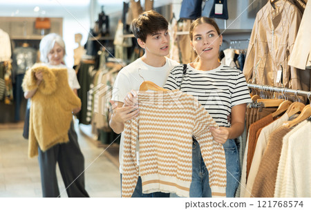 Young girl consults with male friend about purchasing sweater during shopping 121768574