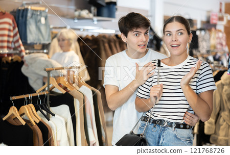Young couple watching excitedly large stock of clothes in clothing store Young couple watching excitedly large stock of clothes in clothing store 121768726