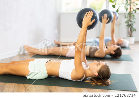 Family grandmother, mother and granddaughter perform fitness exercises lying on floor with softball. 121768734