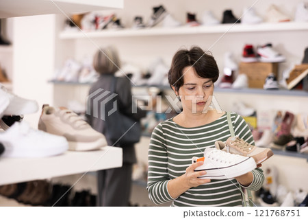 Adult woman chooses sneakers in shoe store 121768751