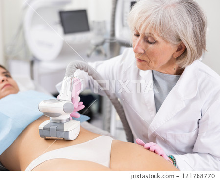 Old woman specialist doing LPG massage of belly of young woman 121768770