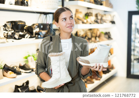 Girl buyer looks at footwear from new collection and picks up new pair of boots for winter. 121768772