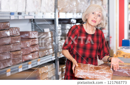 Elderly woman chooses pottery clay in shop Elderly woman chooses pottery clay in shop 121768773