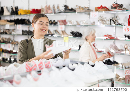 Young woman chooses sneakers in shoe store 121768790