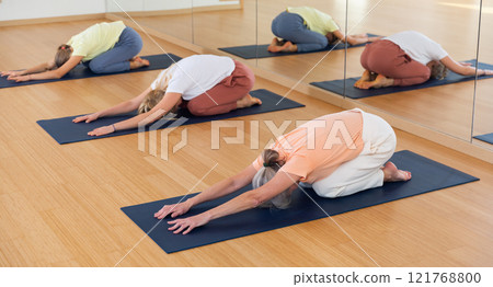Various aged women kneeling in child's pose during group yoga training Various aged women kneeling in child's pose during group yoga training 121768800