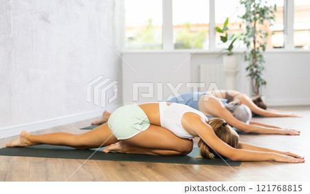 Woman performing Bhujangasana or Cobra pose during yoga class with group in fitness studio Woman performing Bhujangasana or Cobra pose during yoga class with group in fitness studio 121768815