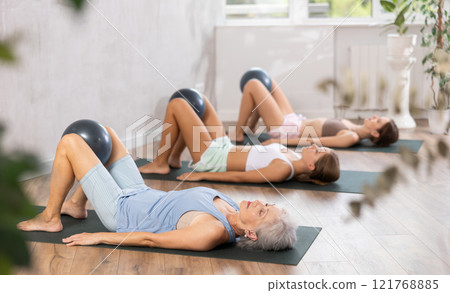 Fitness family in activewear working out with soft ball pilates on mat while doing upper body training in yoga studio Fitness family in activewear working out with soft ball pilates on mat while doing upper body training in yoga studio 121768885