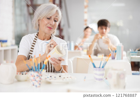 Experienced female artist painting ceramic cup in pottery workshop 121768887