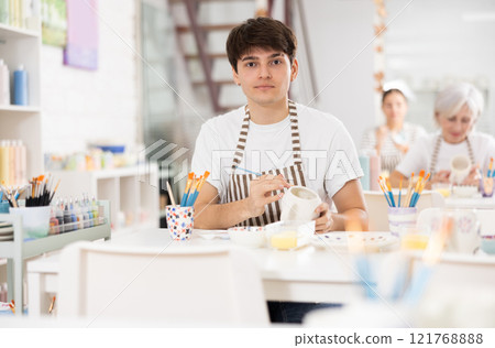 Skilled young artist painting ceramic cup in pottery workshop 121768888