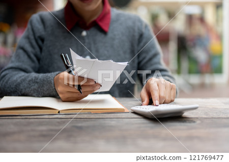 A cropped image of a woman calculating her monthly expenses and bills, using a calculator. 121769477
