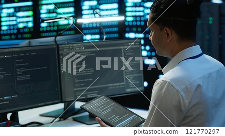 System administrator in data center installing software on computer, troubleshooting issues using tablet. IT staff member in server hub establishing performance benchmarks, camera A 121770297