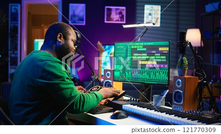 Skilled male composer producing new songs on his mixing console, operating on professional gear in home studio. Artist audio engineer twisting knobs to adjust sound levels on tracks. Camera B. 121770309