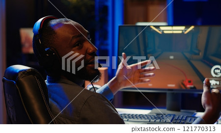 Pro gamer wearing headphones playing game, teaching audience esports needed skills. Content creator in gaming chair talking with audience, filming tutorial on how to defeat enemies, camera A Pro gamer wearing headphones playing game, teaching audience esports needed skills. Content creator in gaming chair talking with audience, filming tutorial on how to defeat enemies, camera A 121770313