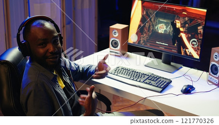 Pro gamer in studio teaching subscribers strategies to beat foes during livestream. Man streaming live from RGB lit living room, recording videogames esports guide for internet audience, camera B Pro gamer in studio teaching subscribers strategies to beat foes during livestream. Man streaming live from RGB lit living room, recording videogames esports guide for internet audience, camera B 121770326