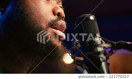 Artist records his voice on microphone in home studio singing a song composed by him. Skilled musician using recordings and lyrics to edit in post production, mixing and mastering session. Camera A. 121770327
