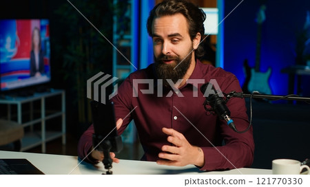 ASMR artist using quality mic and smartphone on tripod in studio to do anti stress video, whispering tingling sounds. Man using microphone and mobile phone to film sleep inducing content, camera A 121770330