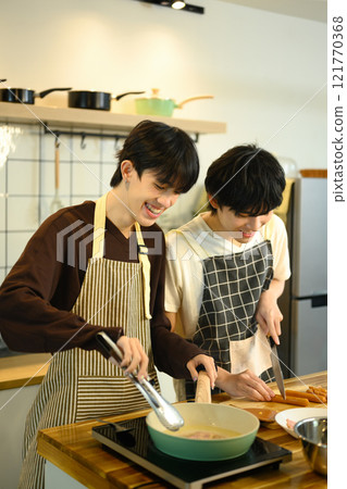Affectionate gay couple wearing aprons preparing meal on the kitchen counter surrounded by fresh ingredients 121770368