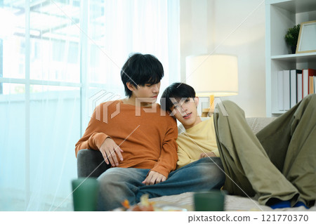 Loving gay couple relaxing together on a comfortable sofa in a bright living room 121770370
