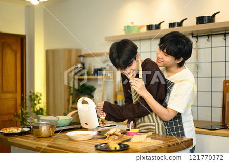 Joyful gay couple sharing a lighthearted moment in the kitchen while preparing food together. 121770372