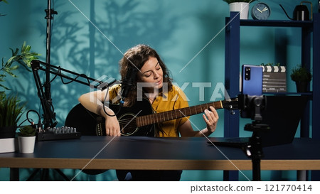 Talented woman playing music on guitar during livestream with audience online. Musician using musical instrument, having fun doing concert for fans producing entertaining songs, camera B Talented woman playing music on guitar during livestream with audience online. Musician using musical instrument, having fun doing concert for fans producing entertaining songs, camera B 121770414