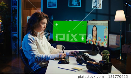 Photo editor using green screen monitor to look at editorial pictures taken with professional camera for fashion magazine. Freelancer browsing images on mockup PC, using graphic tablet, camera B Photo editor using green screen monitor to look at editorial pictures taken with professional camera for fashion magazine. Freelancer browsing images on mockup PC, using graphic tablet, camera B 121770423