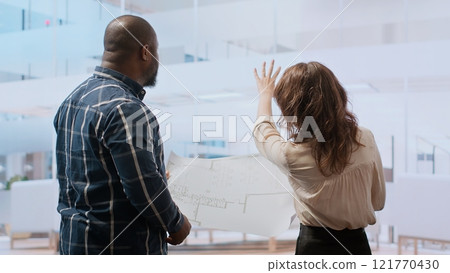 Businesswoman explaining her renovation vision on plans, studying blueprints and discussing layout with the construction manager. Planning a real estate property investment. Camera B. 121770430