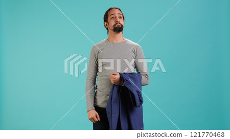 Man holding jacket in one hand while looking around, contemplating, creating a sense of curiosity. Person holding coat showing curiosity for surroundings, studio background, camera A Man holding jacket in one hand while looking around, contemplating, creating a sense of curiosity. Person holding coat showing curiosity for surroundings, studio background, camera A 121770468