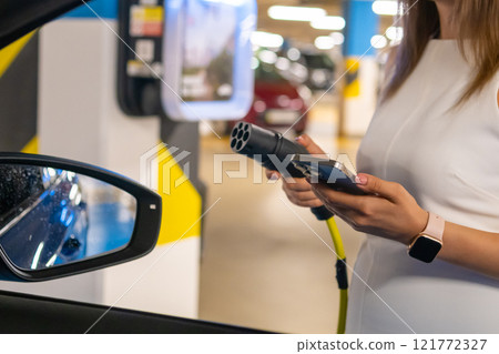 Electric vehicle charging process in a modern parking garage by woman. 121772327