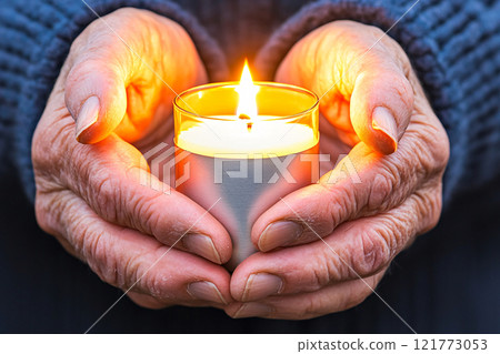 Soft light from a glowing lantern reflects on the faces of hands holding it close 121773053