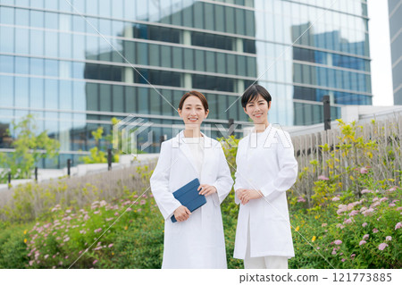 Women in white coats smiling in front of a building 121773885