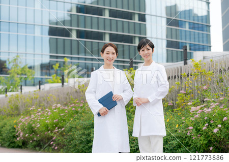 Women in white coats smiling in front of a building Women in white coats smiling in front of a building 121773886