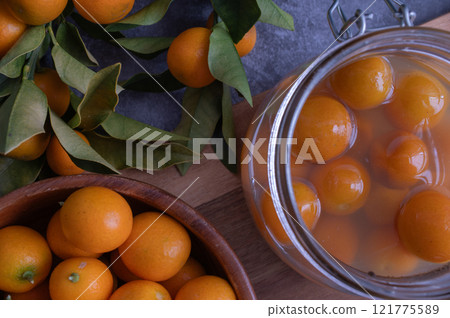 鮮橙色新鮮採摘的金橘和蜜餞金橘放在儲藏罐裡 鮮橙色新鮮採摘的金橘和蜜餞金橘放在儲藏罐裡 121775589
