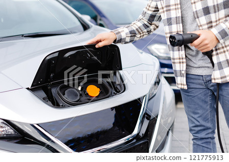 Young man plugging charging cable into the car socket. Electric car charging concept 121775913