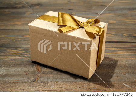 Brown gift box tied with a golden ribbon on a wooden table Brown gift box tied with a golden ribbon on a wooden table 121777246
