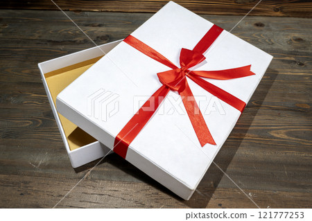 Opening a white gift box tied with a red ribbon on a wooden table 121777253