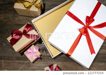 Opening a white gift box tied with a red ribbon on a wooden table 121777254
