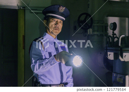 A male security guard guarding a building at night with a flashlight. Photo courtesy of Denpa Gakuen, Tokyo Electronics College. 121779584