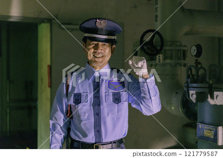 A smiling male security guard guarding a building at night. Photo courtesy of Denpa Gakuen, Tokyo Electronics College. A smiling male security guard guarding a building at night. Photo courtesy of Denpa Gakuen, Tokyo Electronics College. 121779587