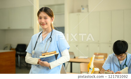 Medical student holding textbooks and smiling confidently at camera Medical student holding textbooks and smiling confidently at camera 121781092