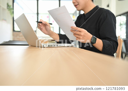 Focused businessman reviewing report while working on a laptop Focused businessman reviewing report while working on a laptop 121781093