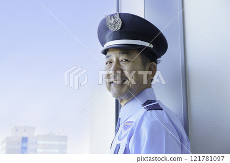 A middle-aged male security guard looking out the window. Photo courtesy of Denpa Gakuen, Tokyo Electronics College. 121781097