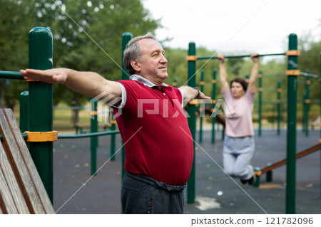 Elderly man doing gymnastics on an outdoor sports ground 121782096