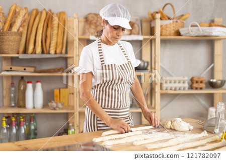 Elderly woman baker rolls out dough 121782097