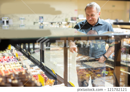 Man chooses cakes at showcase of confectionery department Man chooses cakes at showcase of confectionery department 121782121
