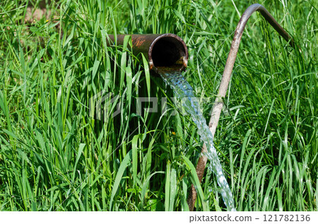 Clear Water Flowing from a Metal Pipe Against Green Grass Clear Water Flowing from a Metal Pipe Against Green Grass 121782136