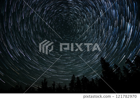 Star trails create mesmerizing circular patterns over a forest at night in a remote location 121782970